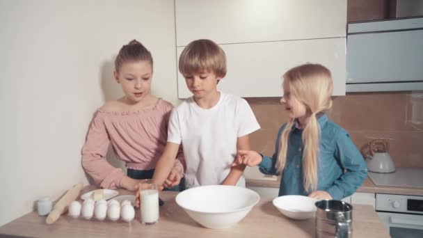Tre barn hjälper till med matlagning i köket. En pojke häller mjölk i en tallrik. — Stockvideo
