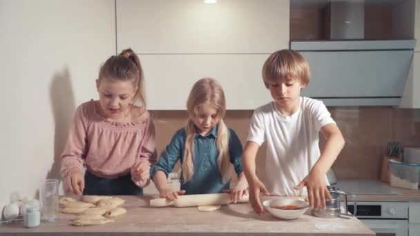 A gyerekek szőkén főznek a konyhában. Gurítsd ki a tésztát egy sodrófával.. — Stock videók