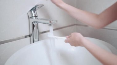 Adamın biri banyodaki temiz bir diş fırçasına diş macunu sürüyor..
