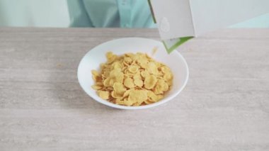 Bir adam beyaz bir tabağa mısır gevreği döker ve süt döker. Uygun beslenme.