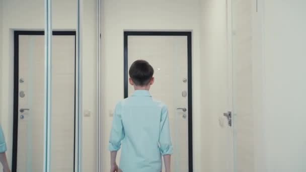 A brunette boy walks out of the light room outside through the door. Blue shirt. — Stock Video
