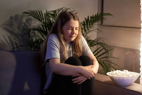 La ragazza con orrore guarda la TV e si spaventa. Guarda un film con i popcorn . — Foto Stock