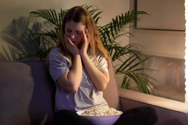 Het meisje met horror kijkt tv en wordt bang. Bekijk een film met popcorn. — Stockfoto