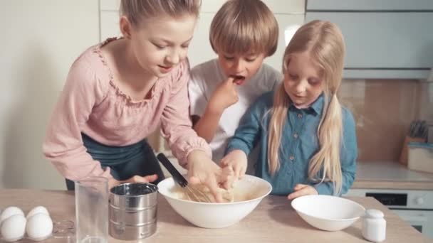 Kinderen bereiden het deeg voor op de taart en proberen het deeg met hun vinger. — Stockvideo