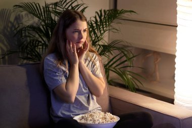 Kanepede oturmuş televizyon izleyen korkmuş bir kız. Samimi oda