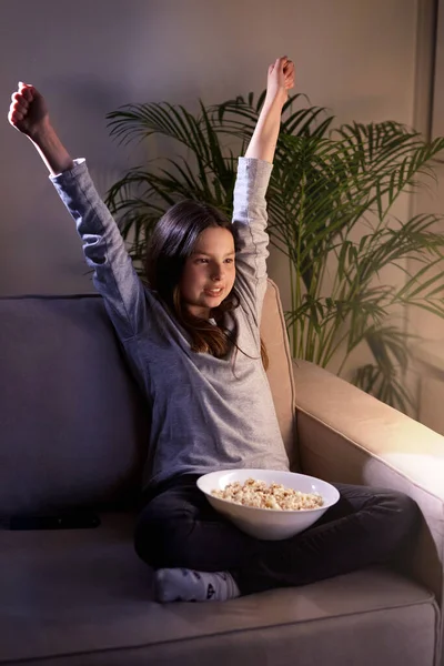 Una linda chica sonriente con ojos marrones está viendo una comedia y comiendo palomitas de maíz . — Foto de Stock