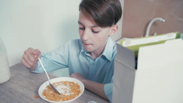 Kleiner brünetter Junge frühstückt Müsli mit Milch vor der Schule. — Stockvideo