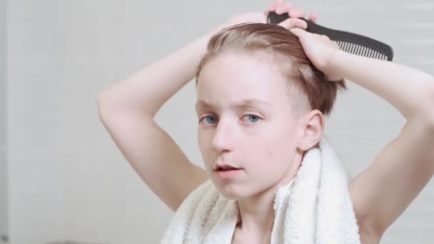 Brunett pojke kammar vått hår nära spegeln. Vit handduk runt halsen. — Stockvideo