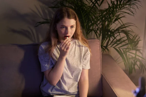 Una ragazza carina che guarda la TV e mangia popcorn. Camera accogliente . — Foto Stock