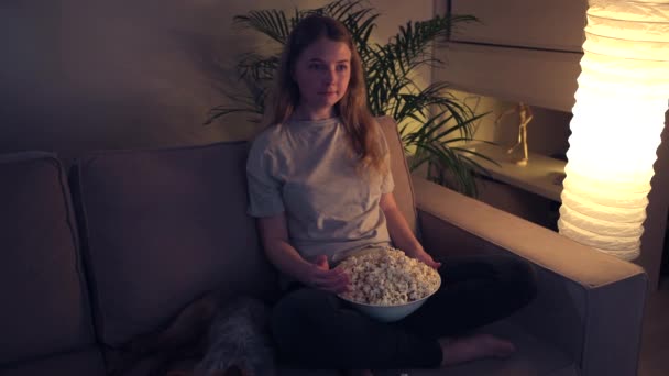 Vacker ung flicka tittar på tv medan du sitter i vardagsrummet. — Stockvideo