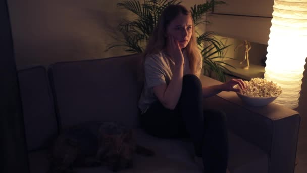 Skrämd flicka tittar på en skräckfilm och äter popcorn. — Stockvideo