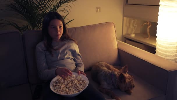 Een glimlachend mooi meisje kijkt tv en eet popcorn. — Stockvideo