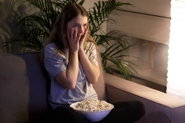Девушка с ужасом смотрит телевизор и боится. Смотреть фильм с попкорном . — стоковое фото