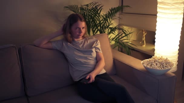 Menina sentada no sofá muda de canais na TV . — Vídeo de Stock