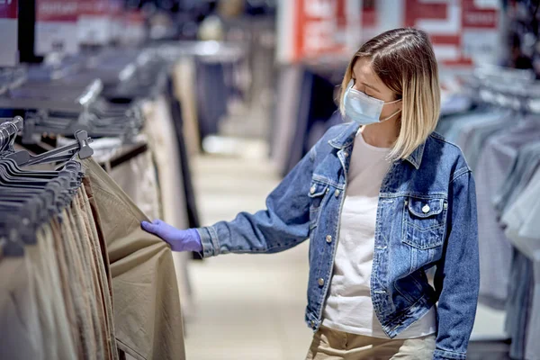 Το κορίτσι κοντά στον καθρέφτη διαλέγει παντελόνια στο εμπορικό κέντρο. Κορίτσι με ιατρικά γάντια. — Φωτογραφία Αρχείου