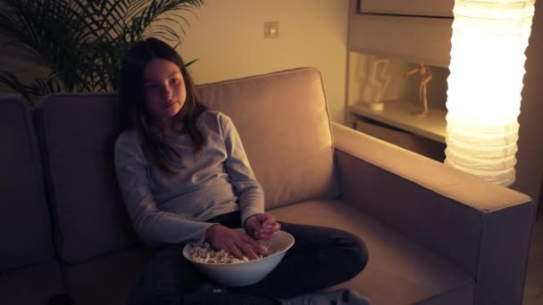 Een mooi meisje kijkt 's avonds tv en gooit popcorn uit angst. — Stockvideo