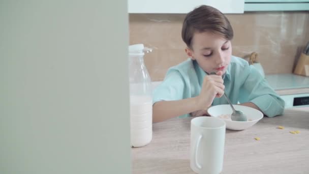 Kleine brunette jongen heeft ontbijt cornflakes met melk in de voorkant van de school. — Stockvideo