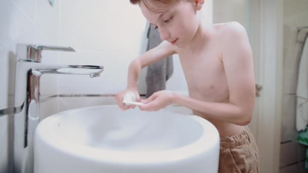 美しいブルネットの少年は歯ブラシとゲルで彼の歯を磨く、ペースト. — ストック動画