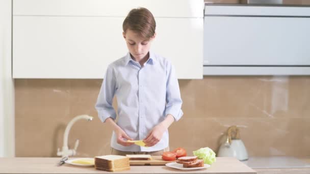 Un chico moreno prepara un sándwich de pan tostado, verduras y queso . — Vídeo de stock