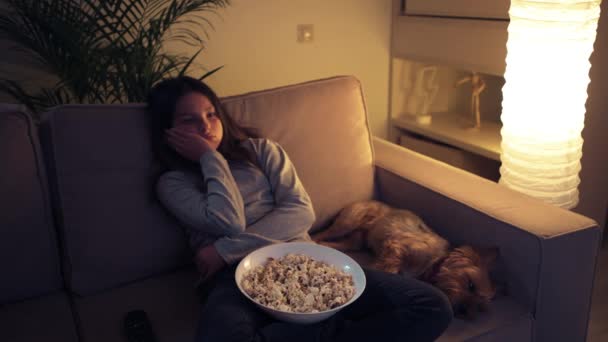 累了的女孩和她的狗坐在沙发上看电视. — 图库视频影像