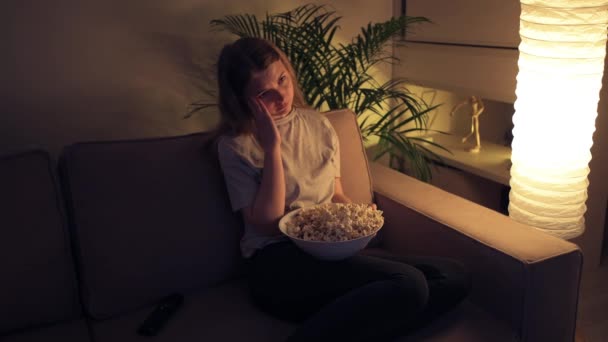 Una chica aburrida está viendo televisión y comiendo palomitas de maíz. . — Vídeo de stock