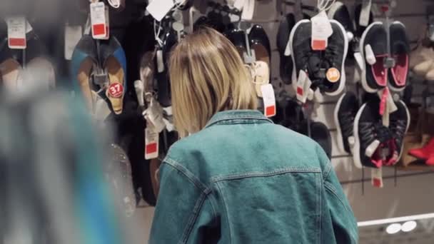Блондинка вибирає взуття в магазині і дивиться на ціни. Безпечні покупки в масці — стокове відео