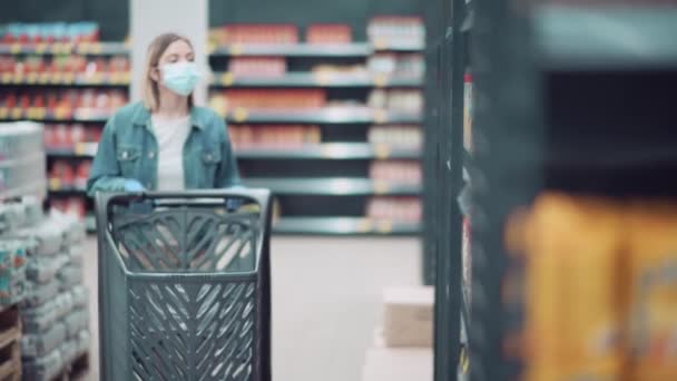 Belle fille blonde dans un masque médical prend des marchandises des étagères à provisions. — Video