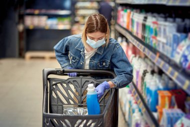 Alışveriş merkezinde maske takan tatlı bir kız sepete bir şeyler koyuyor..