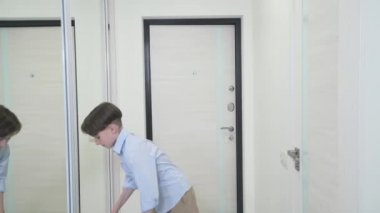 Esmer bir çocuk sırt çantasına bir çanta koyar ve okulun kapısını bırakır..