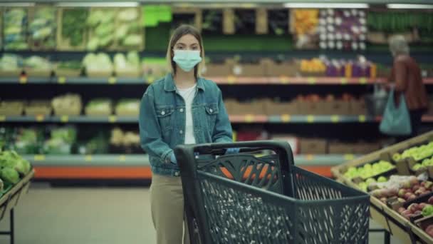 Alışveriş arabalı maskeli sarışın bir dükkanda baş parmak işareti yapıyor.. — Stok video