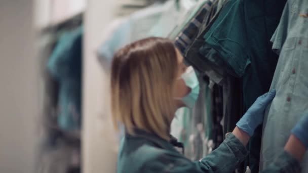 Chica rubia elige ropa, camisa de mezclilla en una tienda. Viaje de compras seguro con máscara — Vídeo de stock