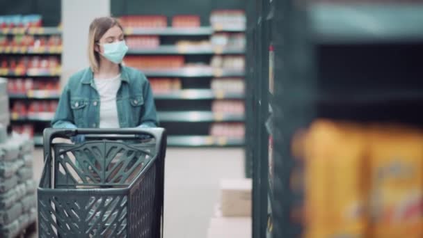 Une fille se promène dans le magasin avec un chariot d'épicerie masqué et des gants. — Video