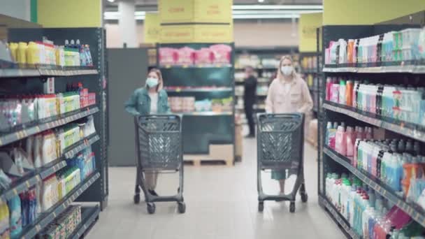 Alışveriş arabalı iki güzel sarışın kız dükkânda yürüyor.. — Stok video