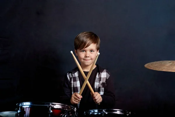 Het kind zit met drumstokken in zijn handen. Studeren in de studio. — Stockfoto