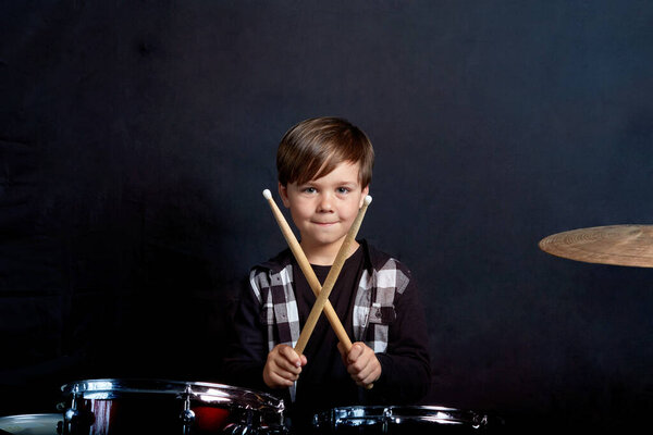 The child sits with drumsticks in his hands. Studying in the studio.