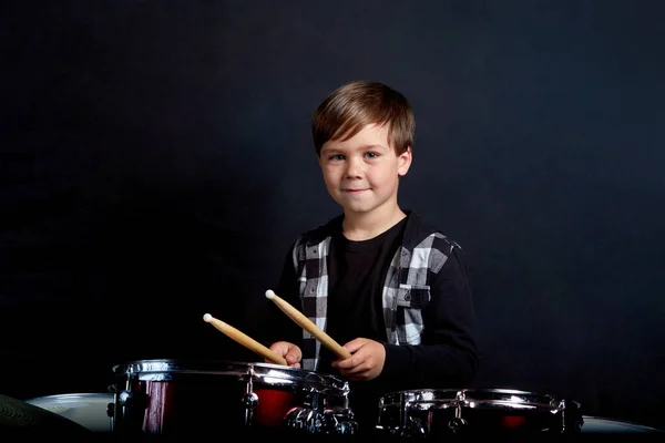 Ett glatt leende barn tittar på kameran och spelar trummor. Pojkar Studios. — Stockfoto