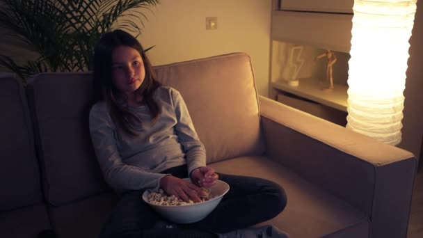 Schattig bang meisje dat een enge film kijkt. Meisje gooit popcorn op de tv. — Stockvideo