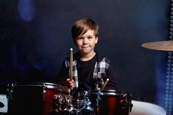 Boy child smiles and looks at the camera playing the drums.