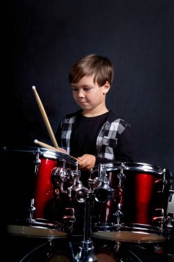 Müzik aleti olan bir çocuğun dikey fotoğrafı, davullar. Koyu mavi arkaplan