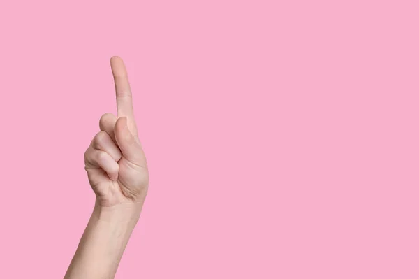 Gyönyörű kaukázusi kéz mutat egy ujjal felfelé. rózsaszín alapon. — Stock Fotó