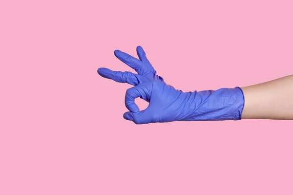 Een hand in een latex chirurgische blauwe handschoen maakt een goed gebaar. op roze achtergrond — Stockfoto