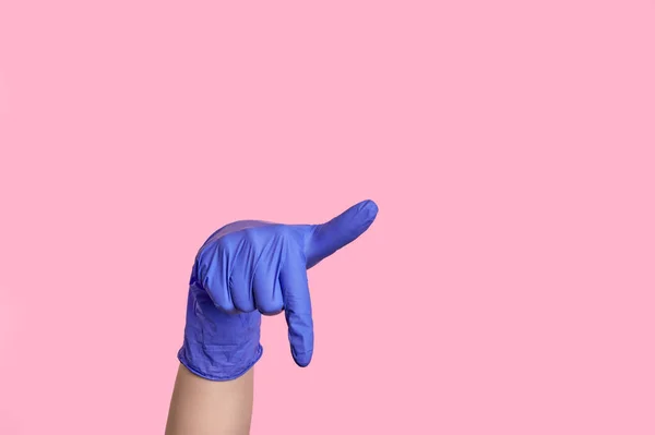 Ένα χέρι σε ένα λατέξ χειρουργικό γάντι δείχνει προς τα κάτω στο κενό χώρο. σε ροζ φόντο — Φωτογραφία Αρχείου