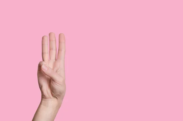 A hármas számú. A női kéz számít az ujjakon. rózsaszín háttér. — Stock Fotó