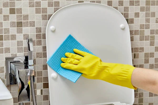 Close-up zonder gezicht het toiletdeksel wassen in beschermende gele reinigingshandschoenen. — Stockfoto