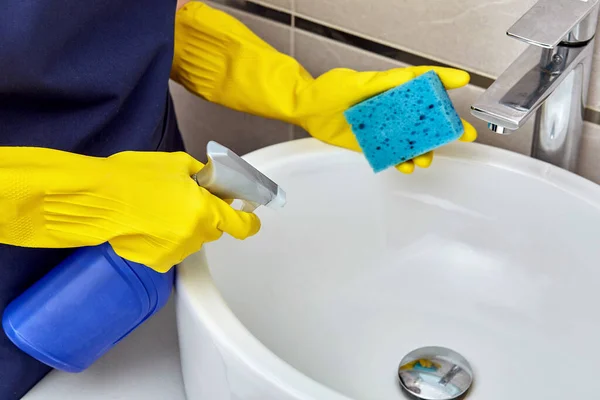 Handen in gele handschoenen voor het reinigen in de buurt van de wastafel in de badkamer. Huisreiniging. — Stockfoto