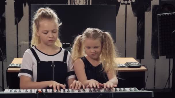 Две девушки играют на синтезаторе. Сестра учит играть на музыкальном инструменте . — стоковое видео