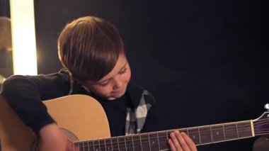 Güzel, gülümseyen esmer çocuk akustik gitar çalıyor. Koyu arkaplan.