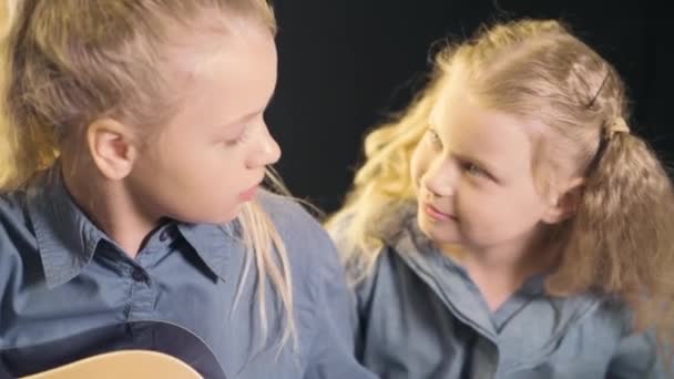 Dos hermosas hermanas jóvenes con el pelo ondulado aprenden a tocar la guitarra . — Vídeos de Stock