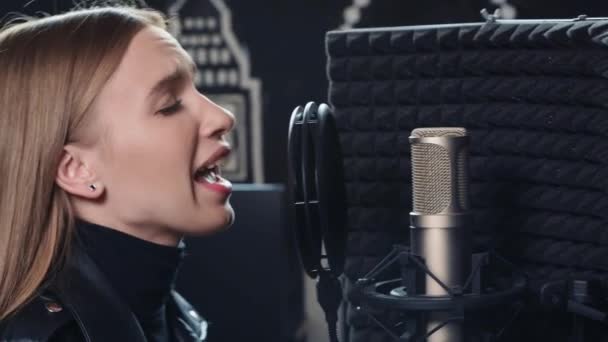 Fiatal szőke lány érzéssel énekel egy mikrofonba. — Stock videók