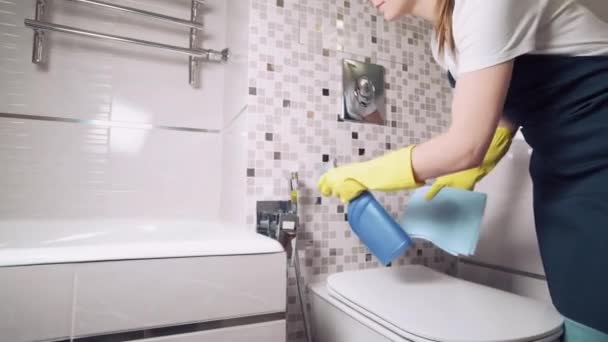 Uma menina em luvas de borracha faz a limpeza no banheiro e lava um bidé. — Vídeo de Stock